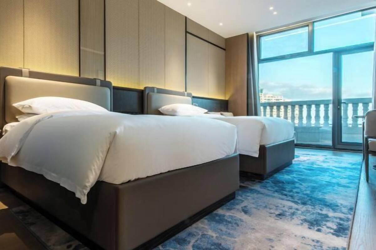 Une chambre d’hôtel avec un grand lit, un plus petit lit, un balcon avec une balustrade et une vue sur un immeuble.