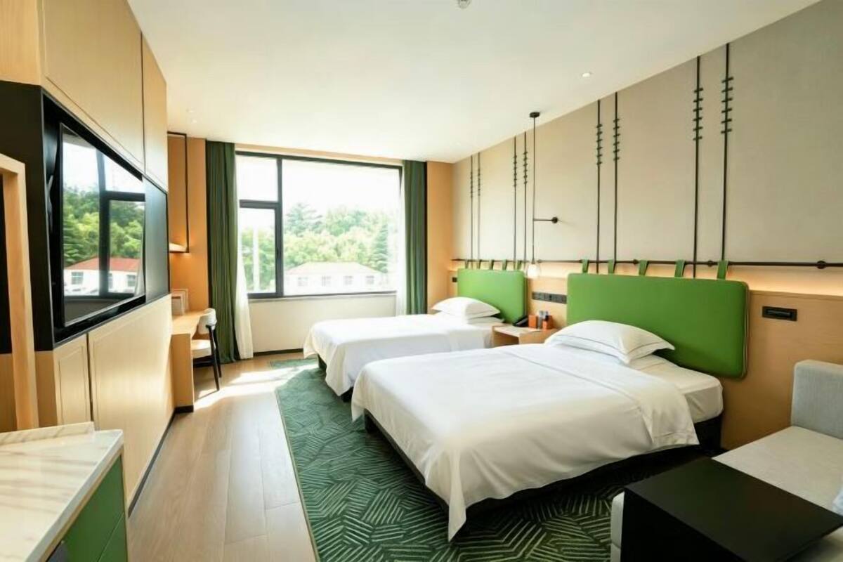 Une chambre d’hôtel avec deux lits, un bureau, une télévision et une grande fenêtre avec des rideaux.