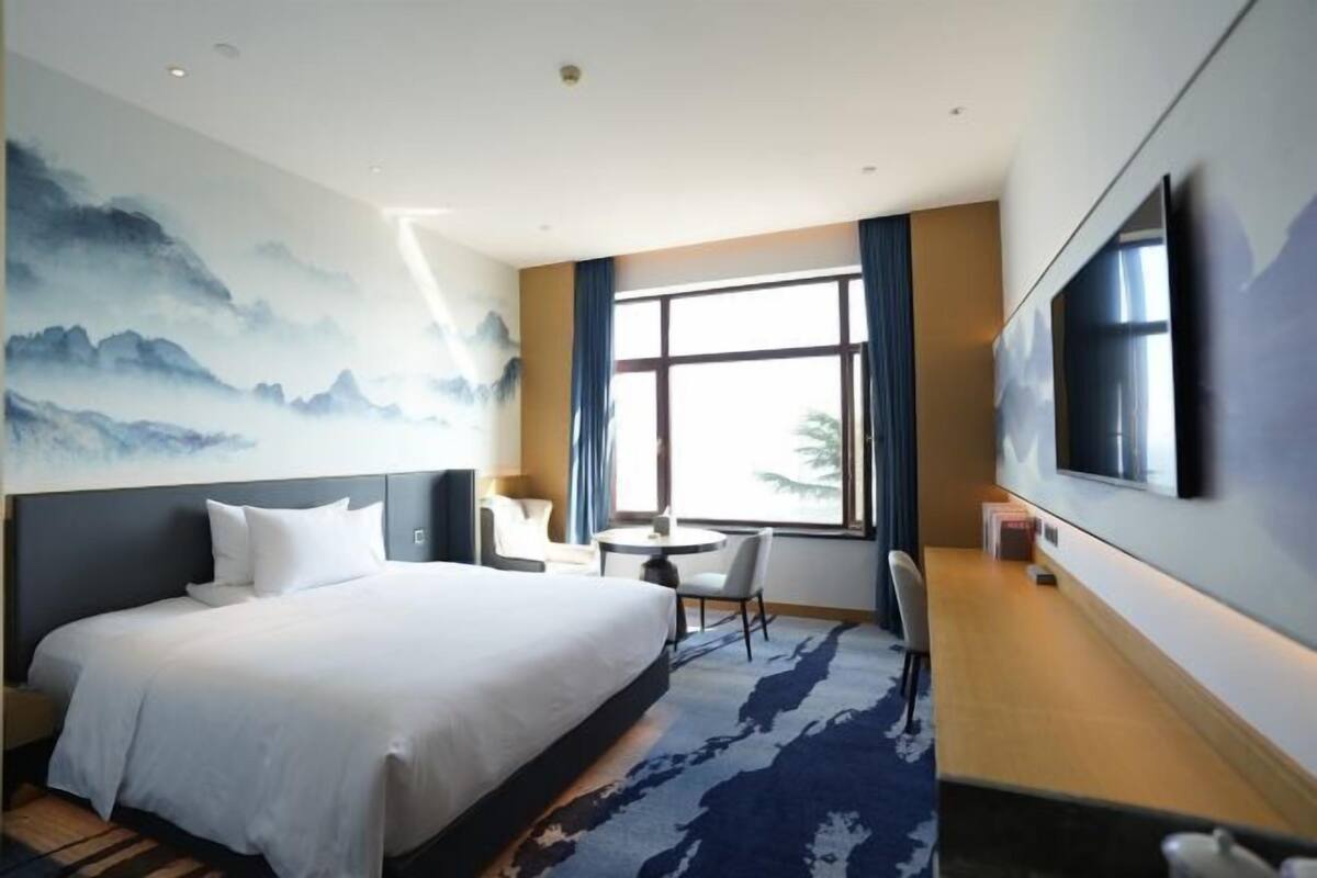 Une chambre d’hôtel avec un grand lit, un bureau, une chaise, une télévision et une fenêtre avec des rideaux.