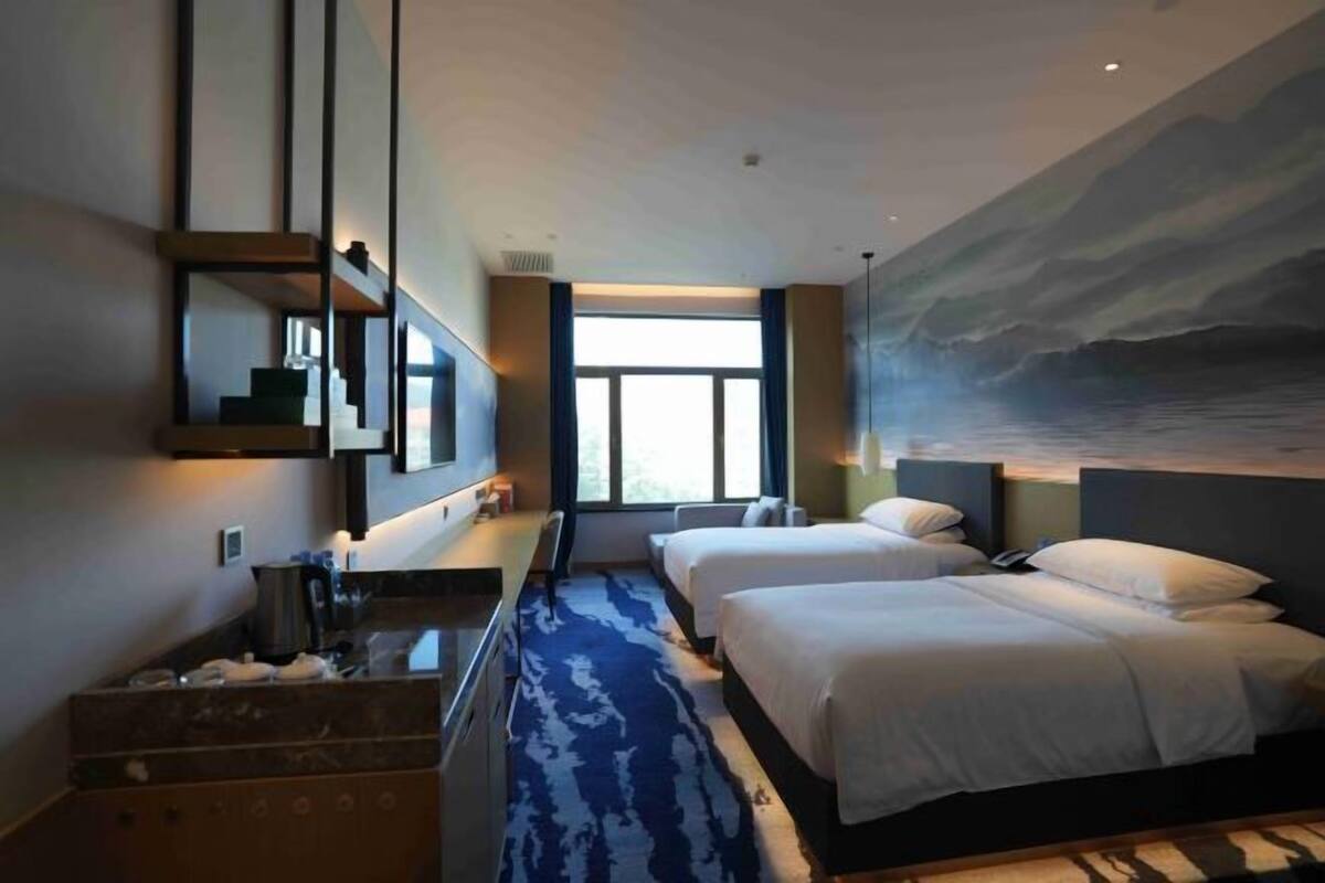Une chambre d’hôtel avec une grande fenêtre, un lit, un bureau et un tableau au mur.