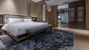 A modern bedroom with a large bed, a bench, a dark patterned rug, wooden panel walls, and a sliding glass door leading to a balcony. - Weihai Dongshan Hotel (Weihai)