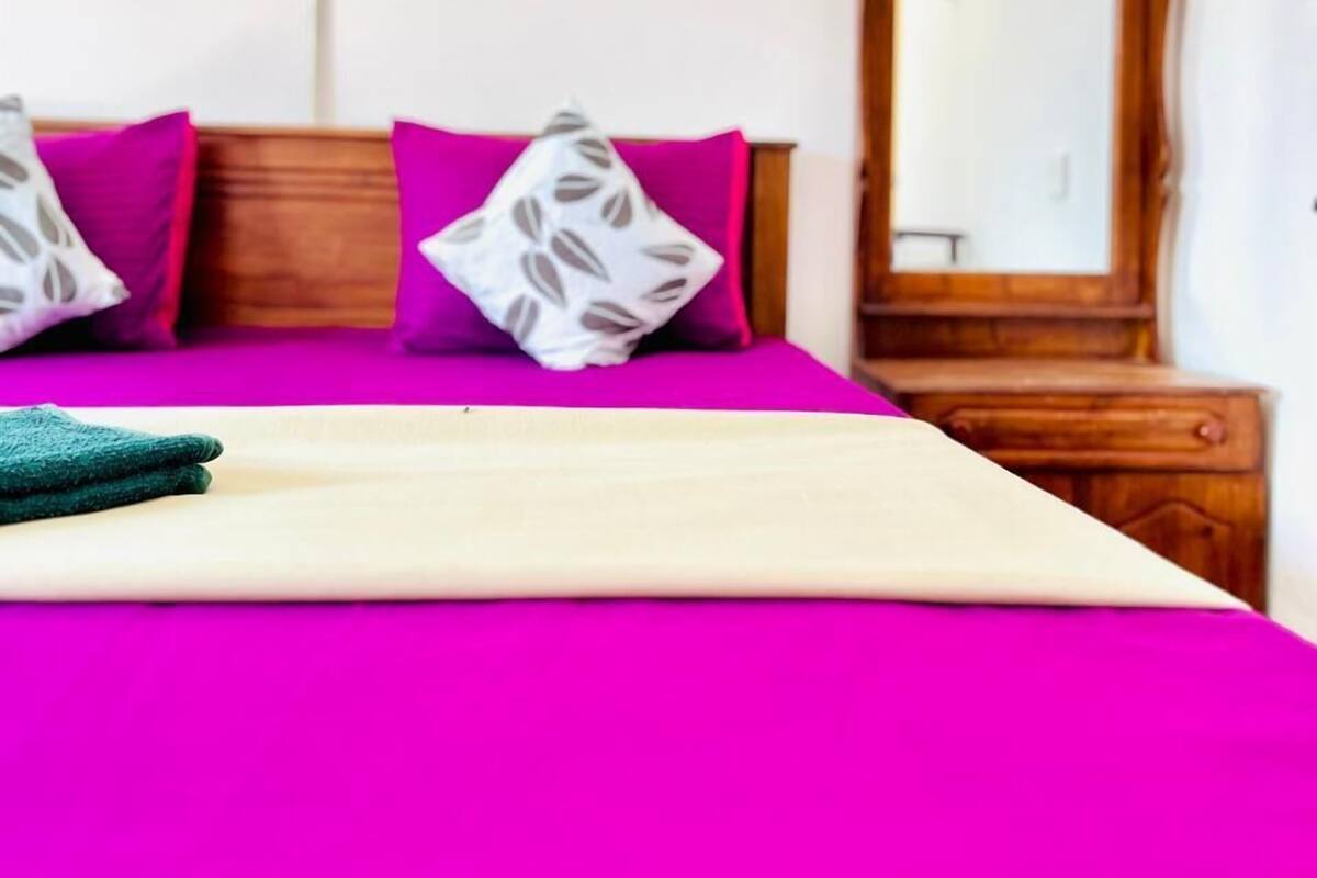 A bed with a bright pink bedspread and two pillows, one with a leaf pattern.