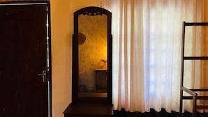 A room with a wooden door, a mirror, a chair, and a window with curtains. - Nethu freedom cottage (Ahangama)