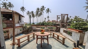 A rooftop terrace with a round table and benches, surrounded by palm trees and a view of the sea. - Nethu freedom cottage (Ahangama)