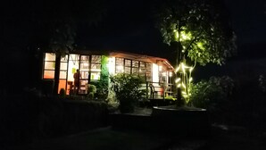 A building with large windows and a balcony, surrounded by greenery and illuminated by string lights. - OP Village Resort (Ravi Opi)