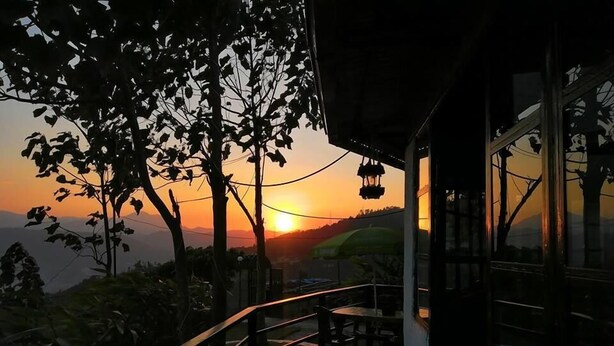 A wooden deck with a railing, overlooking a sunset view with trees and distant hills. - OP Village Resort (Ravi Opi)