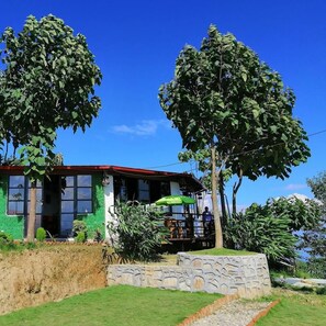 Stunning two-story building with a green facade and red roof, featuring large windows and a balcony with a green umbrella.