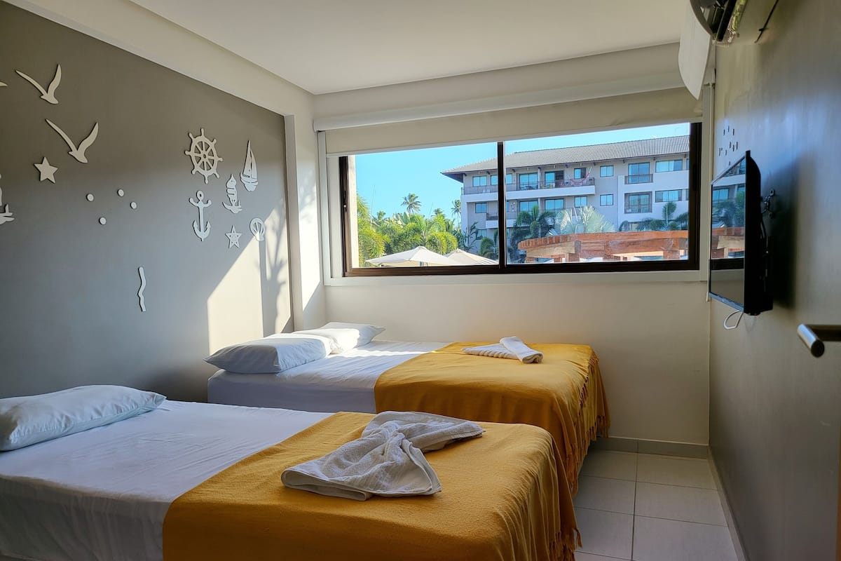 A hotel room with two beds, a large window, and a view of a building outside.