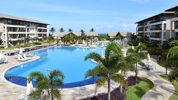 A resort with a large swimming pool, multiple balconies, and palm trees. - Eco Life Porto De Galinhas (Ipojuca)