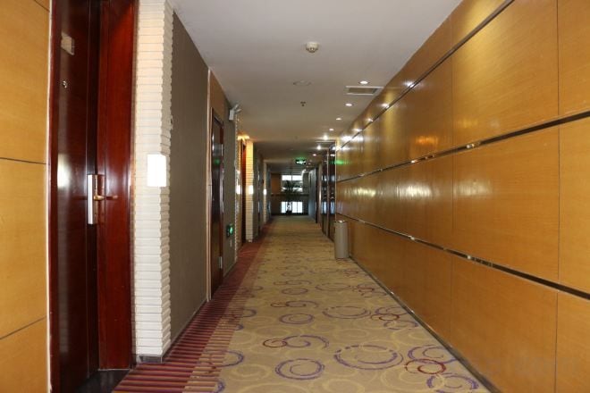 Un couloir d’hôtel avec un tapis à motifs, des murs en bois et une série de portes.