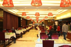 Un ristorante con diversi tavoli e sedie, lampade pendenti rosse e un lungo bancone.