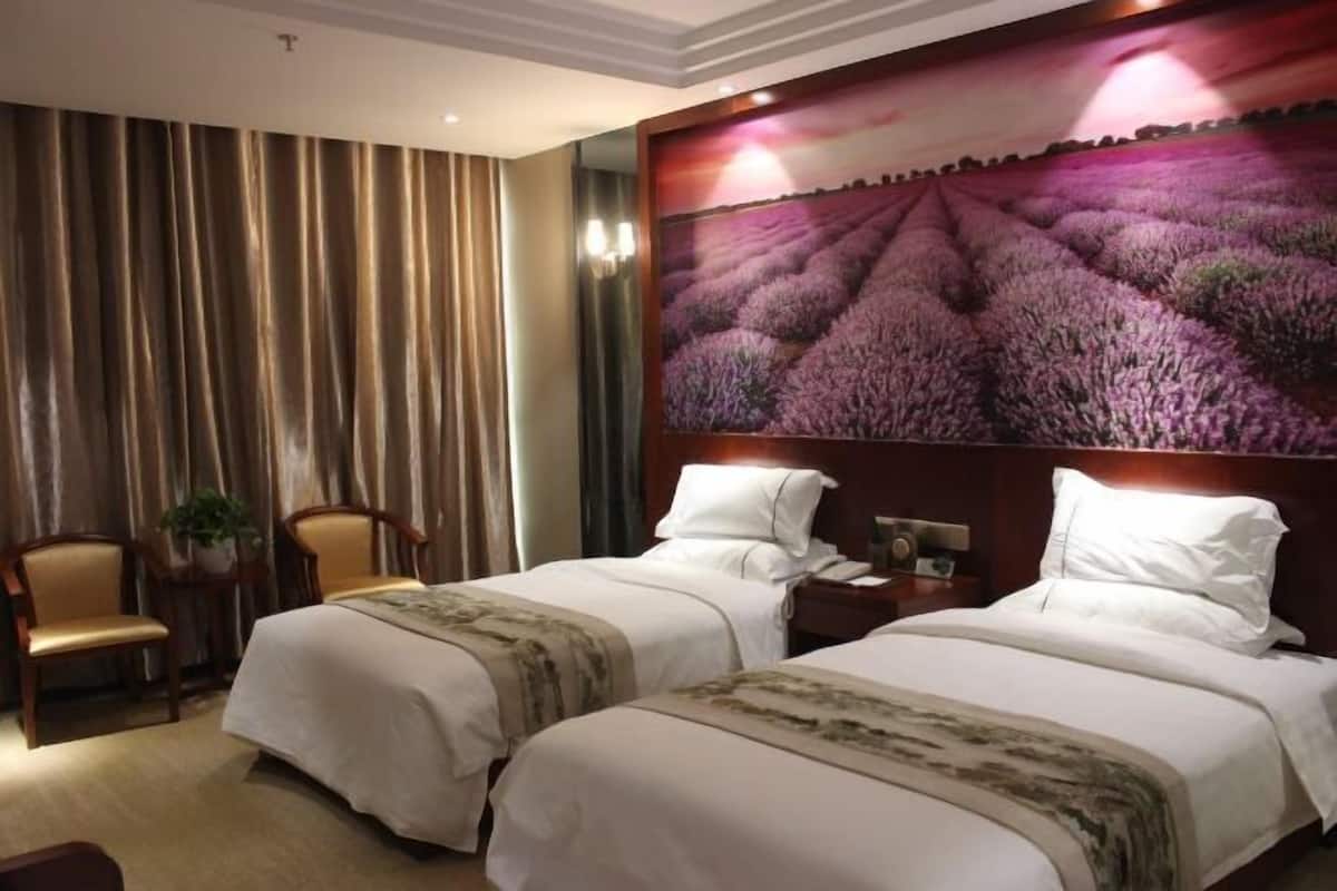Une chambre d’hôtel avec deux lits, un grand tableau représentant des champs de lavande, un lustre et une vue sur le paysage urbain.