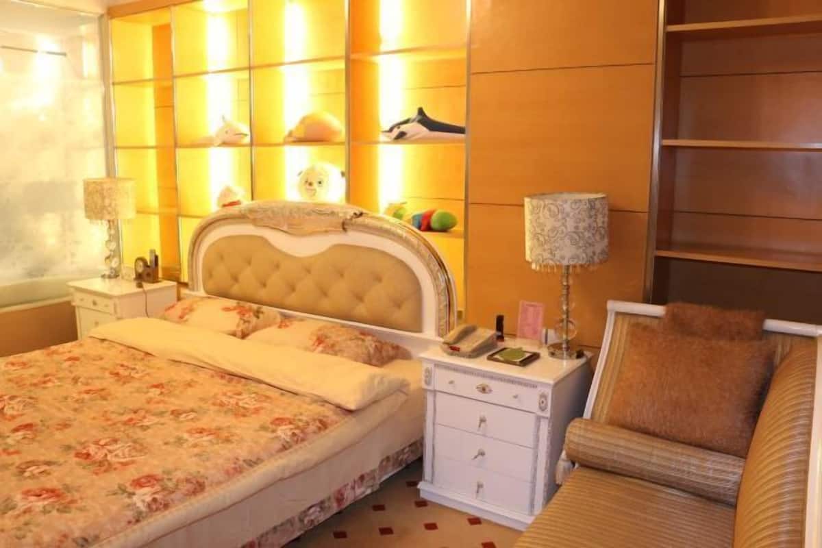 Une chambre d’hôtel comprenant un lit, des tables de chevet, une lampe, une chaise et une étagère avec divers objets.