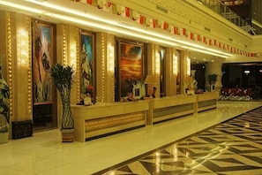 Een hotel lobby met een receptiebalie, groot kunstwerk in een lijst en een incheckbalie.