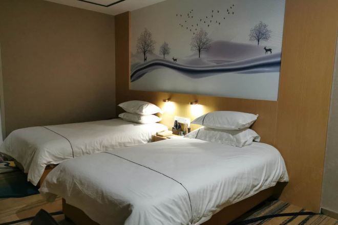 Habitación de hotel con dos camas, una mesita de noche con lámparas y un mural en la pared con un paisaje.