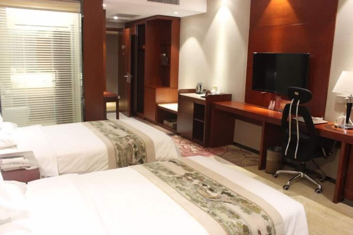 Une chambre d’hôtel avec deux lits, un bureau, une chaise, une télévision et une fenêtre avec des stores.