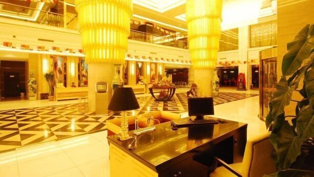 Een ruime lobby met een receptiebalie, grote decoratieve lampen en een vloer met een geometrisch patroon.