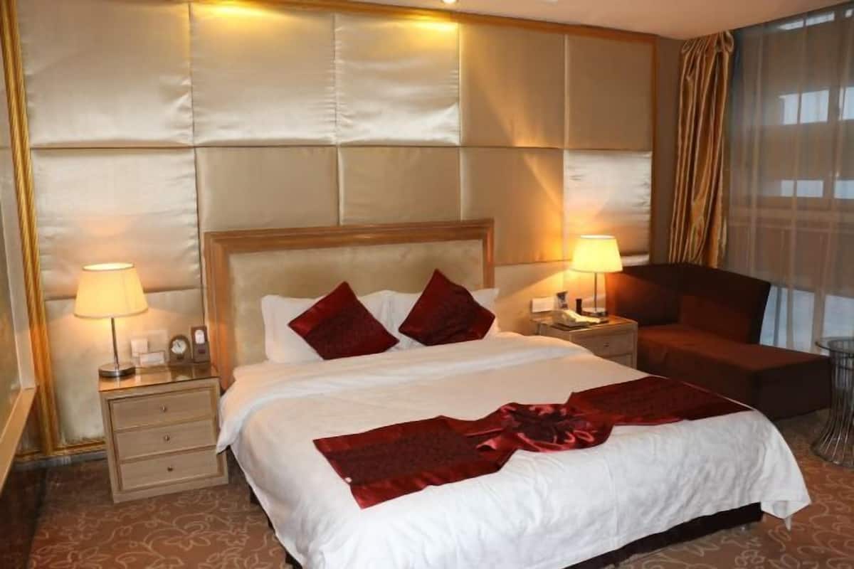 Une chambre d’hôtel avec un grand lit, deux tables de chevet, une petite table d’appoint, un plaid rouge et une vue sur la ville.