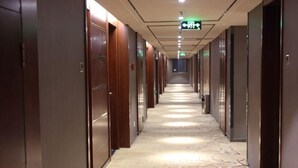 Een hotelgang met deuren aan beide kanten, een kamerbreed tapijt en een nooduitgang.'