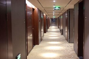 Corredor de hotel com portas em ambos os lados, um tapete estampado e um sinal de saída de emergência.