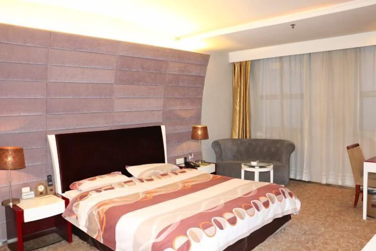 Une chambre d’hôtel avec un lit, un bureau, une chaise, une lampe et une fenêtre avec des rideaux.