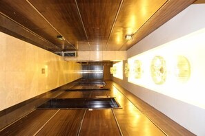 A corridor with wooden flooring, recessed lighting, and wall-mounted light fixtures. - Zheng Tai He East Hotel (Liaocheng)