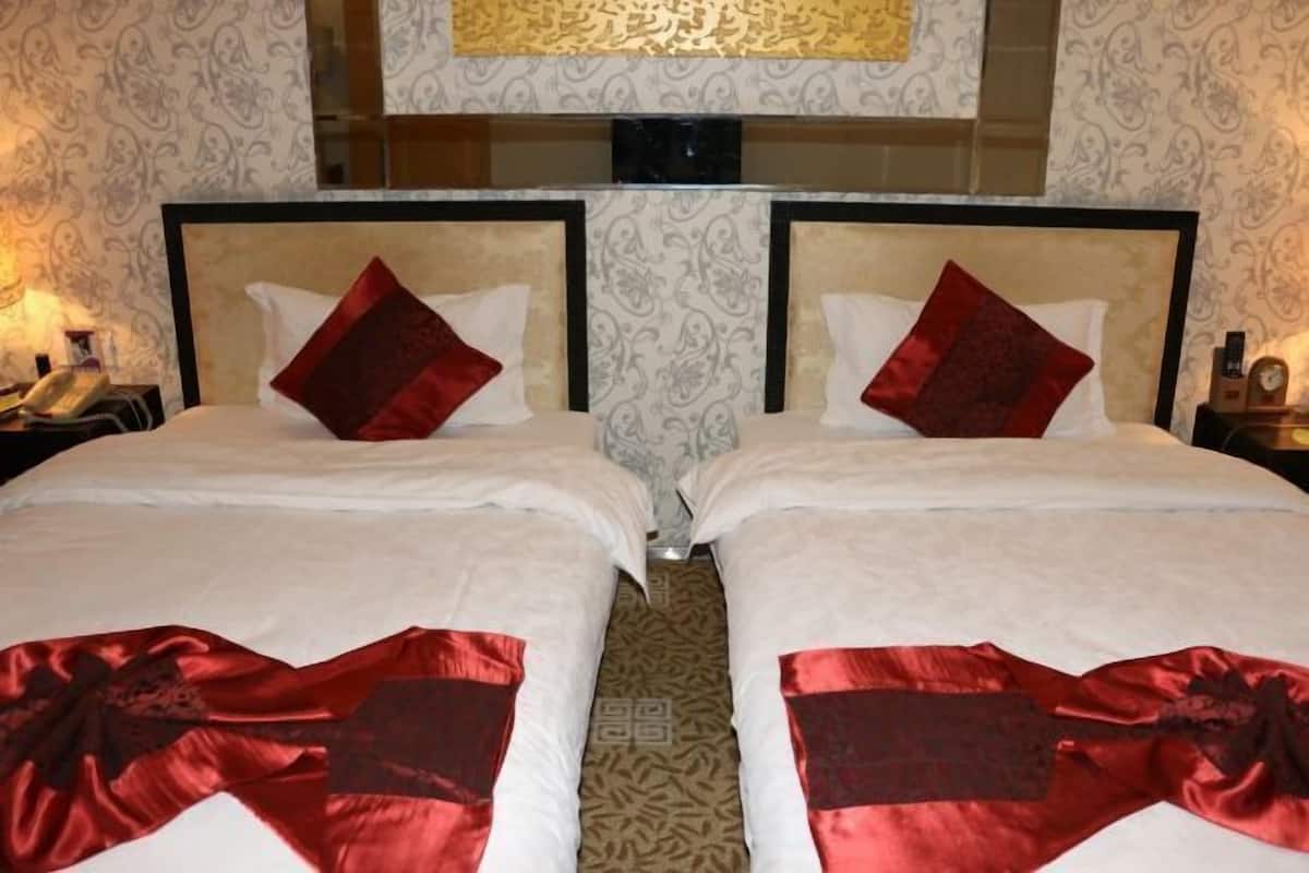Une chambre d’hôtel avec deux lits, chacun agrémenté d’un coussin rouge et d’un tissu décoratif rouge placé au pied du lit.