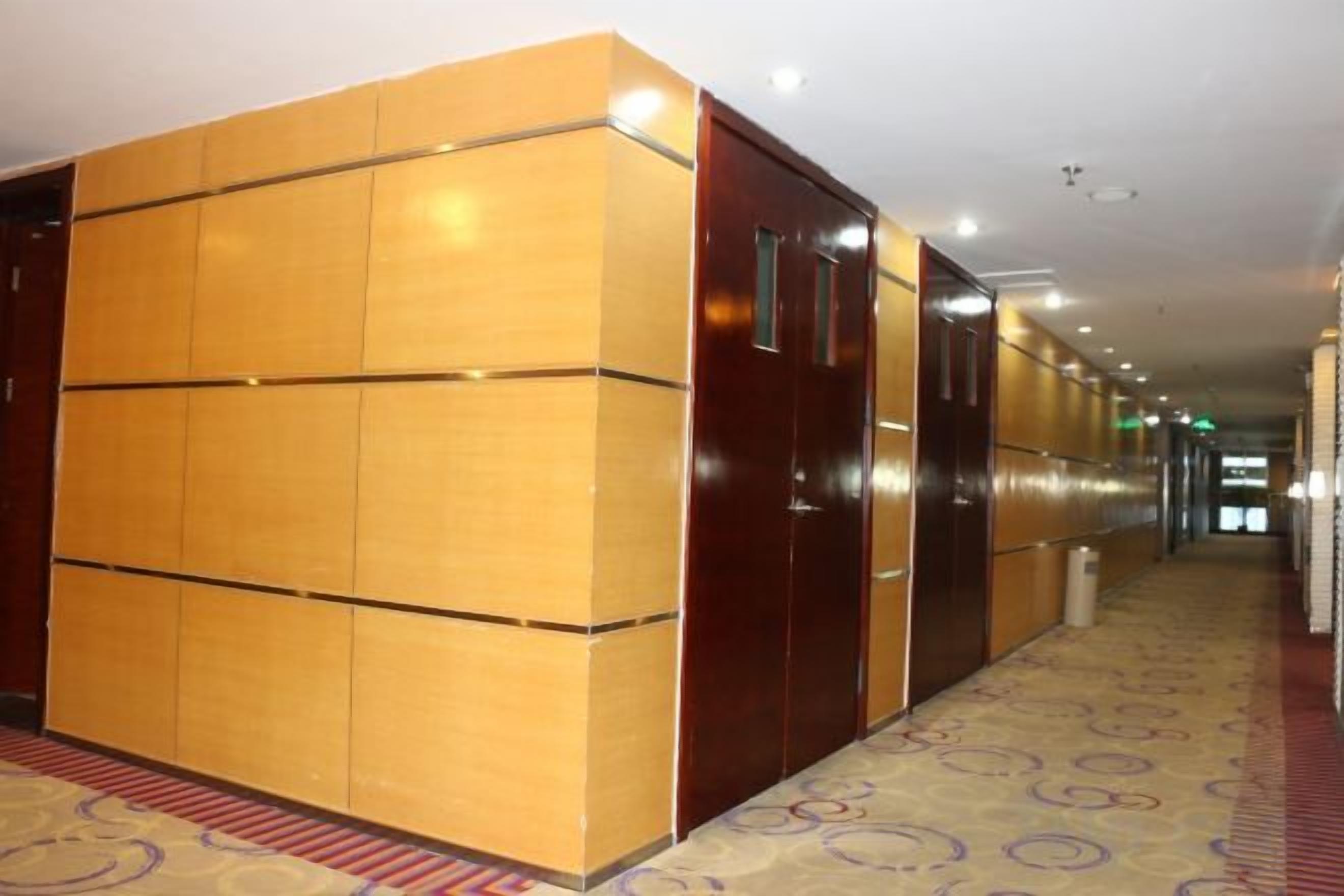 A hotel corridor with wooden paneling, a patterned carpet, and a red carpeted area.