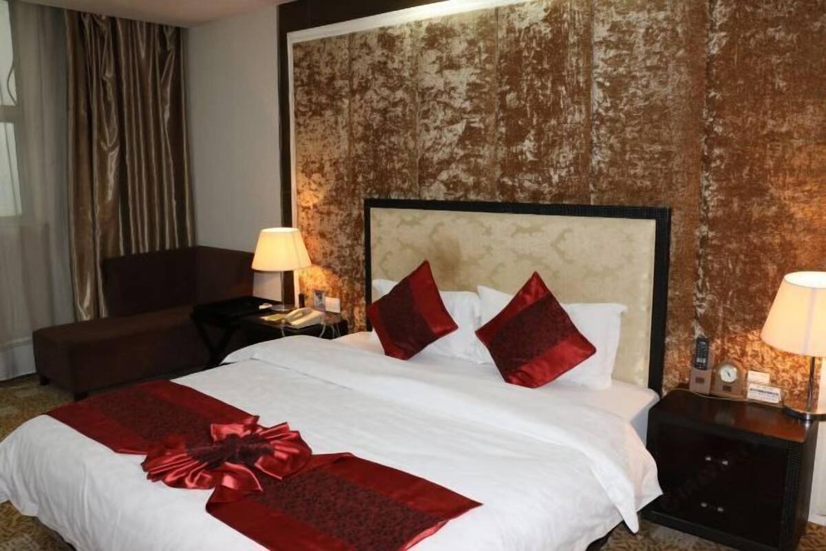 Une chambre d’hôtel avec un grand lit, deux tables de chevet, une petite table, une chaise et un rideau.