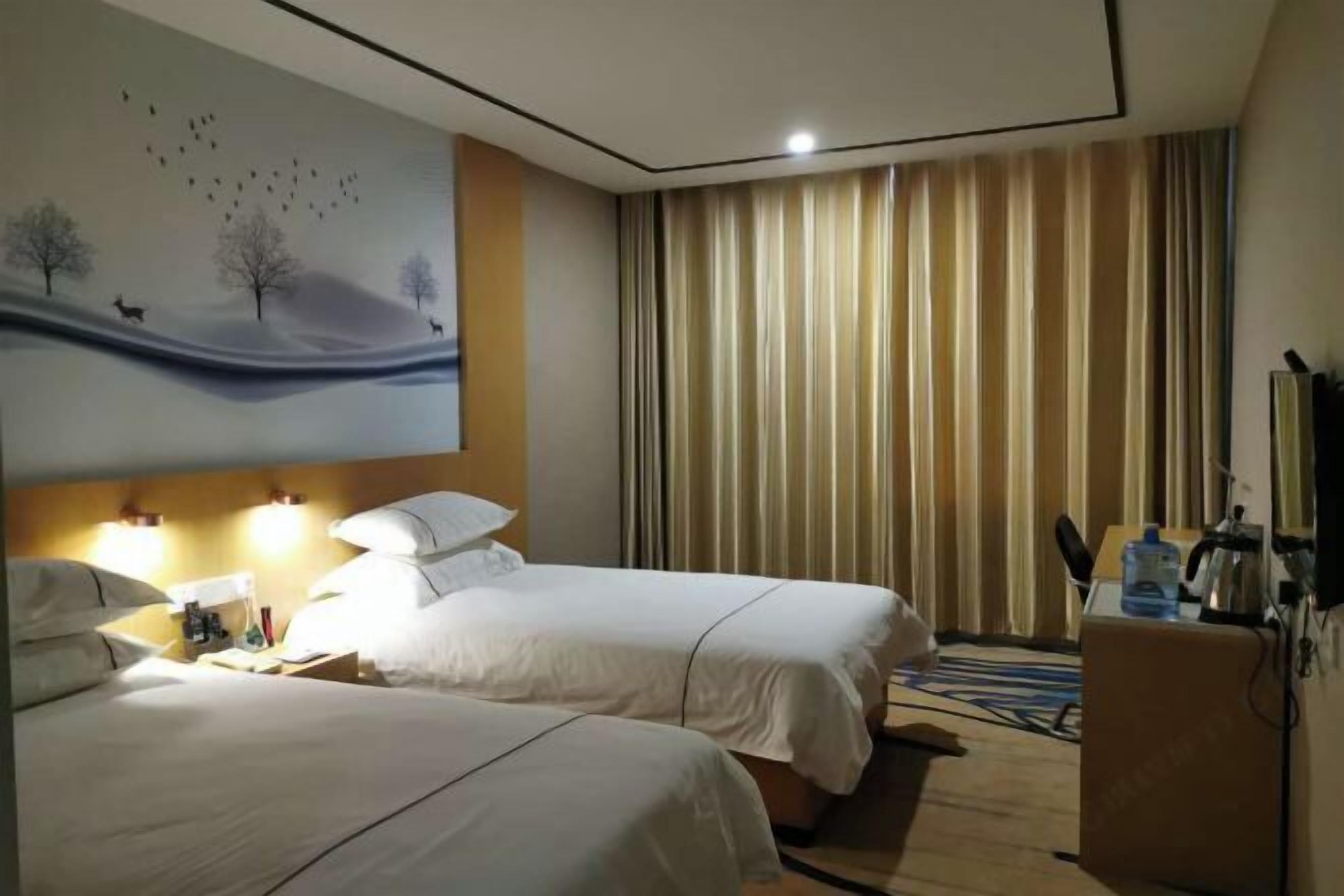 A hotel room with two beds, a painting of a landscape, a desk with a lamp, and a view of the outside through curtains.