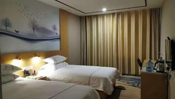 Habitación de hotel con dos camas, un cuadro de un paisaje, un escritorio con una lámpara y vistas al exterior a través de cortinas.