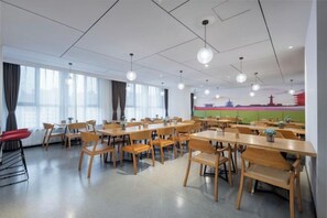 A dining area with tables and chairs, large windows, and a mural on the wall.
