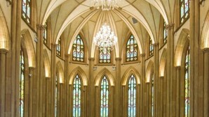 Interno di una cattedrale con soffitti a volta, vetrate colorate e un lampadario centrale.