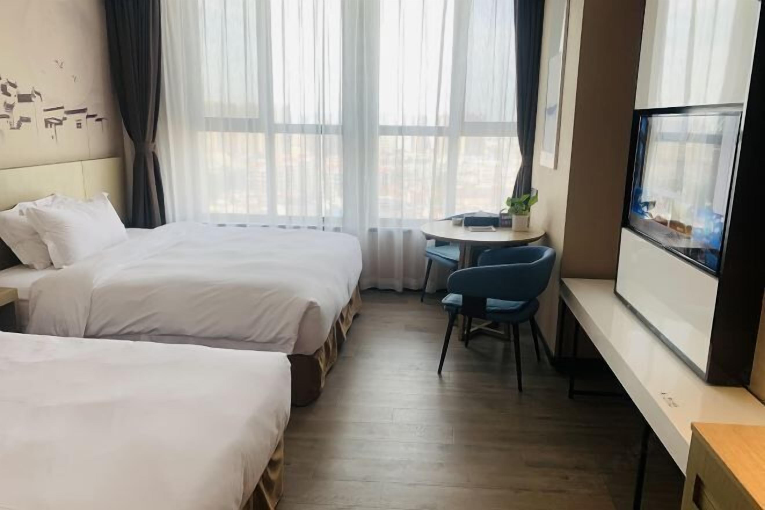 A hotel room with two beds, a small desk with a chair, a TV, and a window with curtains.