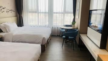 A hotel room with two beds, a small desk with a chair, a TV, and a window with curtains.