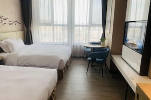 A hotel room with two beds, a small desk with a chair, a TV, and a window with curtains.