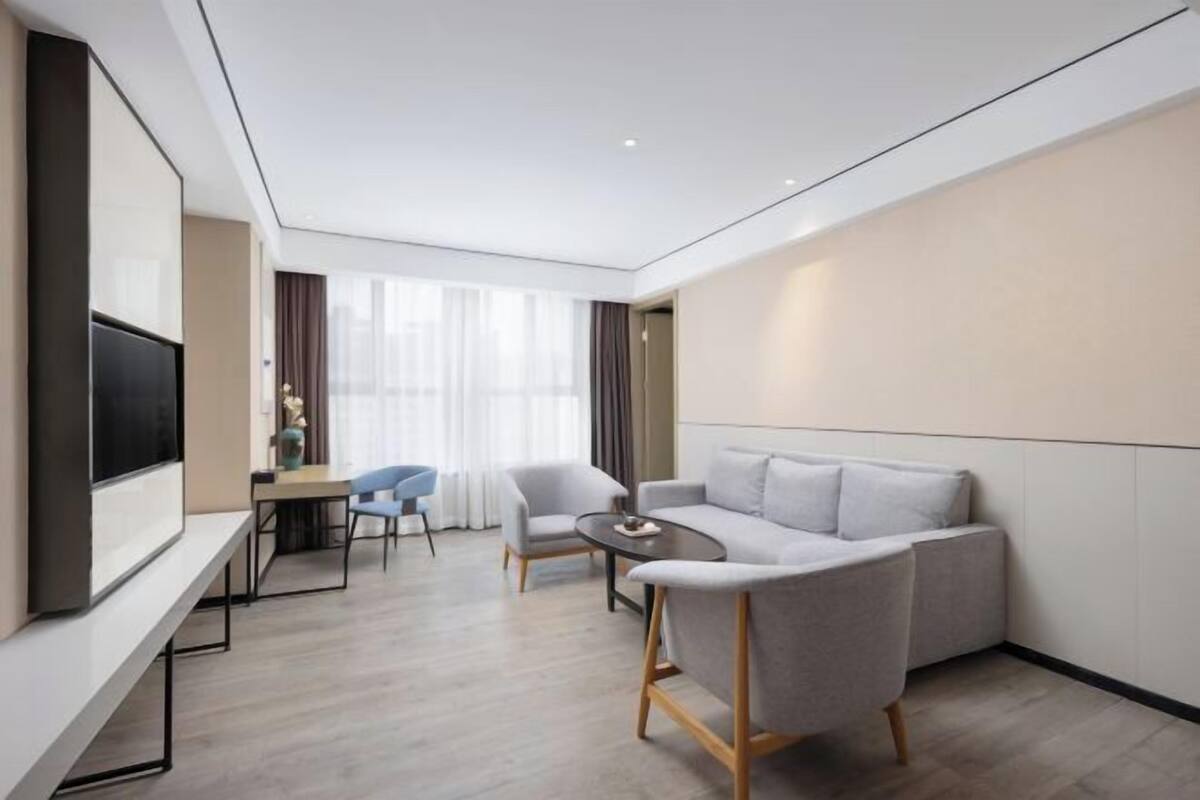 A modern hotel room with a sofa, a small table, a TV, and a window with curtains.