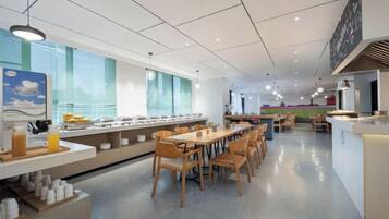 Una cafetería amplia con mesas y sillas largas, una zona de bufé y un mostrador con un menú.