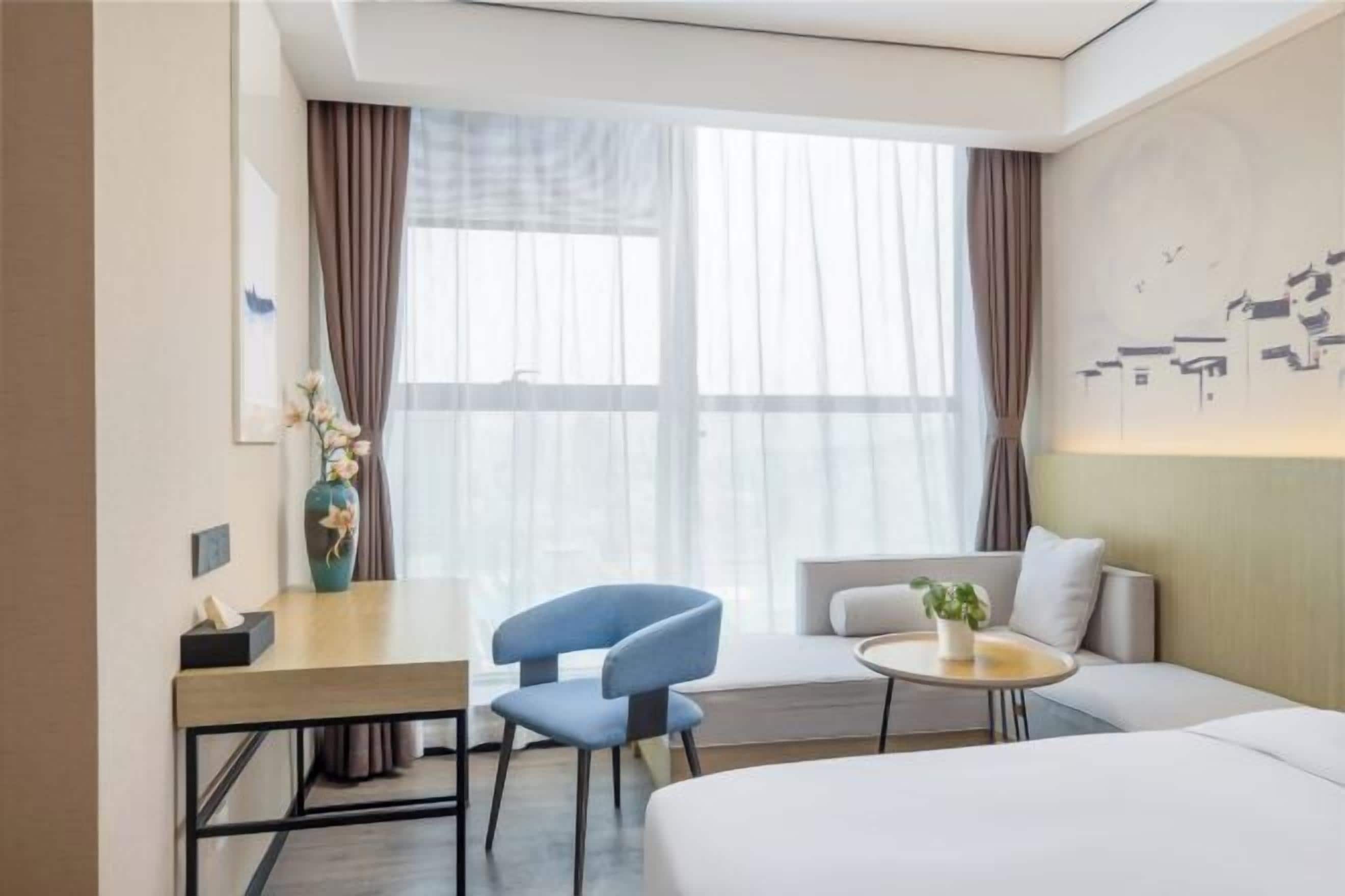 A hotel room with a bed, a desk, a chair, a small round table, and a window with curtains.