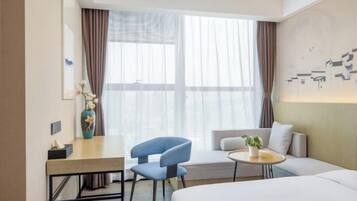 A hotel room with a bed, a desk, a chair, a small round table, and a window with curtains.