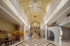 A grand hotel lobby with a high ceiling, a central staircase, and a reception desk. - Grace Select Hotel (Yantai South Street Railway Station) (Yantai)