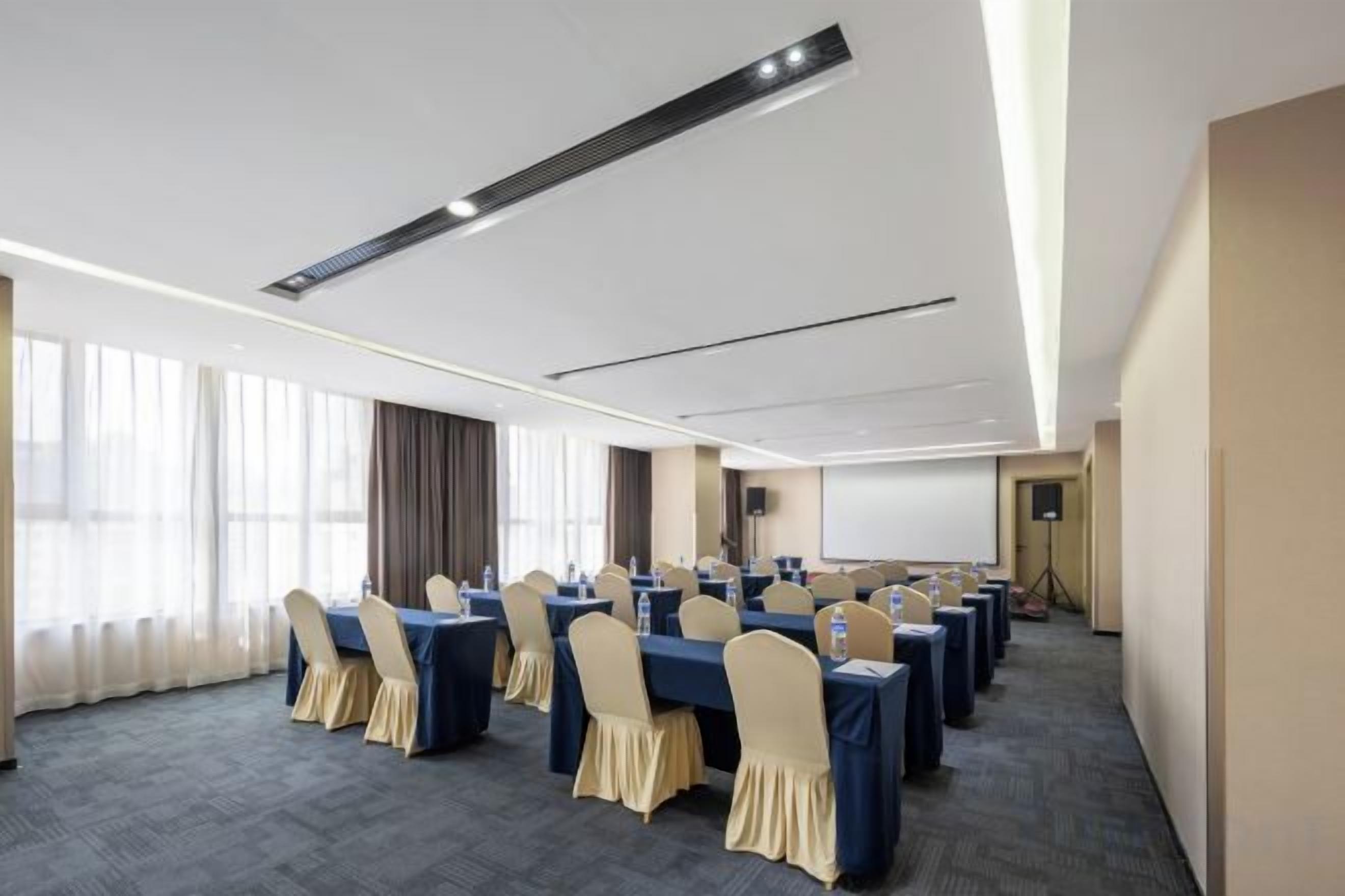 A conference room with multiple tables and chairs, a projector screen, and a large window with curtains.
