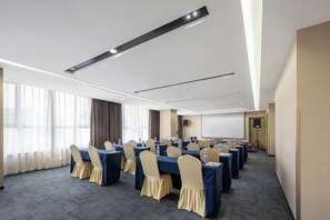A conference room with multiple tables and chairs, a projector screen, and a large window with curtains.