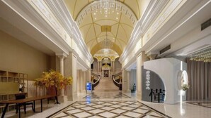 Un'imponente hall d'hotel con pavimento in marmo, una scalinata centrale e un lampadario.