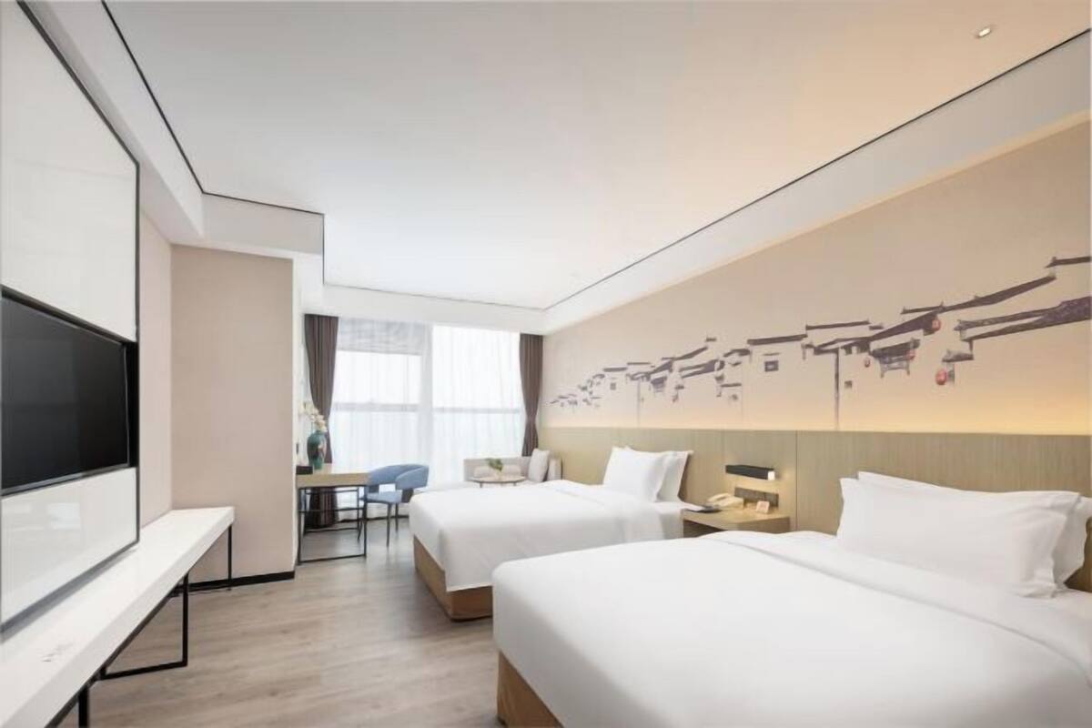 A hotel room with two beds, a TV, a desk, and a chair.