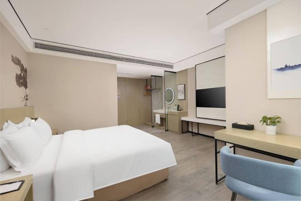 A modern hotel room with a bed, desk, chair, and a large mirror.
