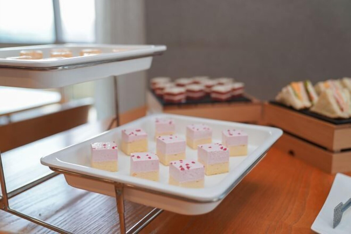 A tray of square-shaped desserts with pink frosting and sprinkles on a white tray.