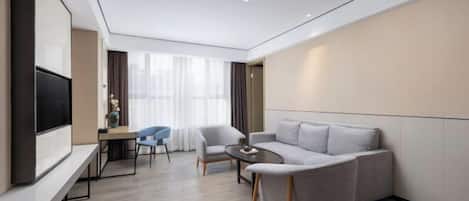 A modern hotel room with a sofa, a dining table with chairs, a flat-screen TV, and a large window with curtains.