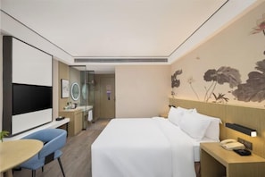 A modern hotel room with a large bed, a desk with a chair, a TV, and a bathroom visible through a glass door.