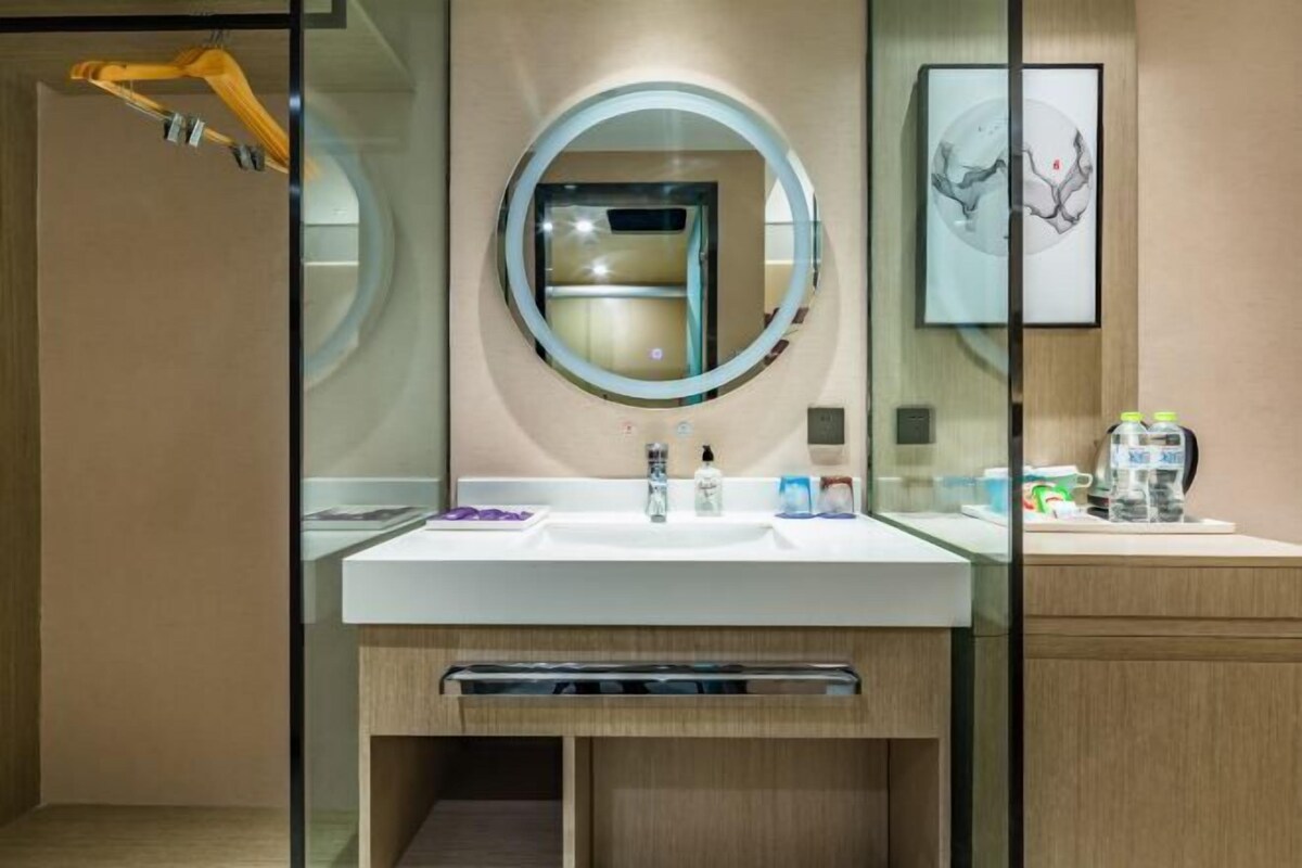 A modern bathroom with a large mirror, a white sink, and a wooden cabinet.